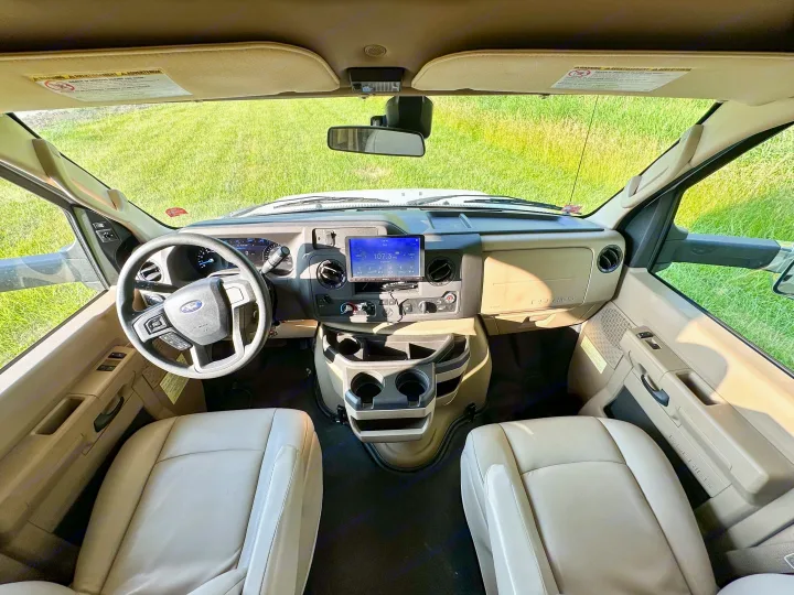 RV rental interior. View from inside the Ford E-Series cab, showing the steering wheel, dashboard, and beige front seats.. Winnebago Minnie Winnie 2021