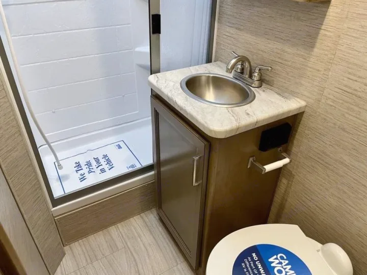 Inside a compact RV rental bathroom featuring a shower, vanity with sink, and toilet. Ready for your journey.. Thor Coleman 2022