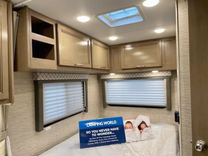 Spacious RV rental bedroom with wood cabinets, two windows, and a bed. A ceiling skylight brightens the space.. Thor Coleman 2022