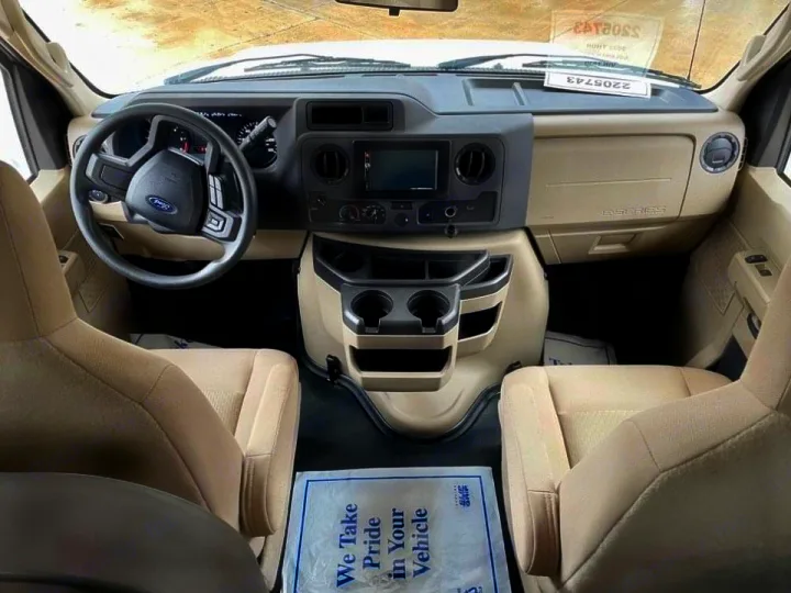 Front cockpit view of an RV rental: Beige seats, black dashboard, steering wheel, and central console visible.. Thor Coleman 2022