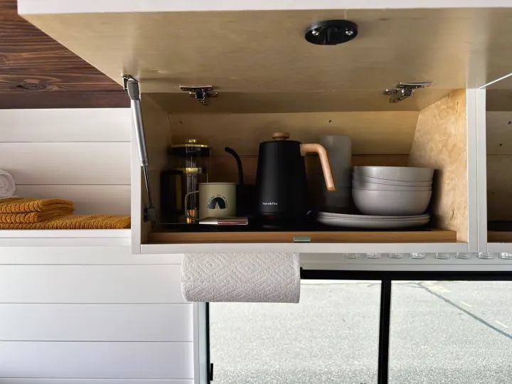RV rental kitchen setup: an open cabinet reveals a kettle, French press, and dishes, ready for your travel adventures.. RAM ProMaster 2500 2022