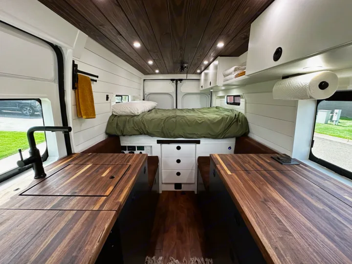 Explore this stylish RV rental interior: wooden ceiling, white shiplap walls, full bed, and functional kitchen with wood counters.. RAM ProMaster 2500 2022