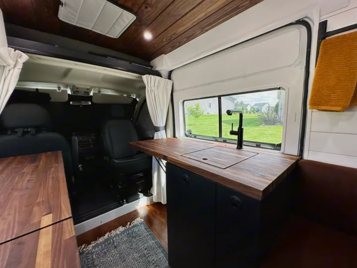 Explore this RV rental's cozy interior, featuring a wood-finished kitchen, sink, and comfy seating in a sleek camper van.. RAM ProMaster 2500 2022
