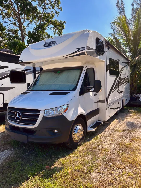 Bright white Mercedes-Benz Class C RV rental, a Jayco Melbourne motorhome, sitting on gravel under a clear sky.. Jayco Melbourne 2022