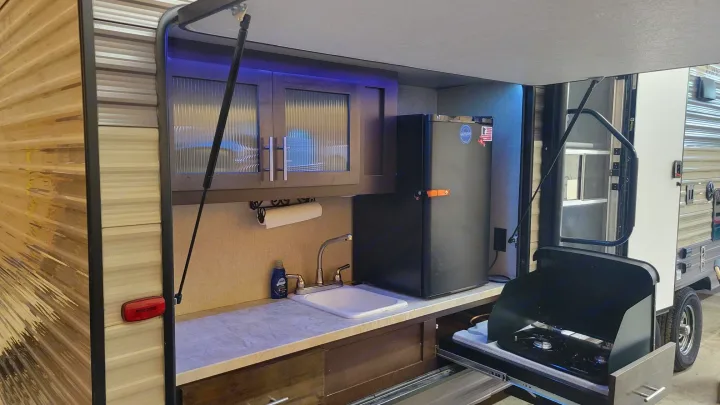 RV rental outdoor kitchen with sink, pull-out stove, fridge, and cabinets featuring purple LED lighting.. Forest River Cherokee Grey Wolf 2017