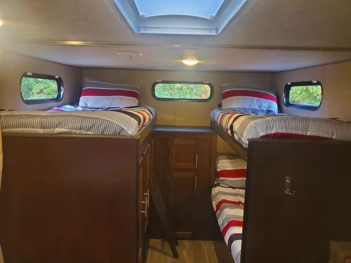 Cozy RV rental interior with four striped bunk beds, a skylight, and windows showing trees. Ideal for family adventures.. Forest River Cherokee Grey Wolf 2017