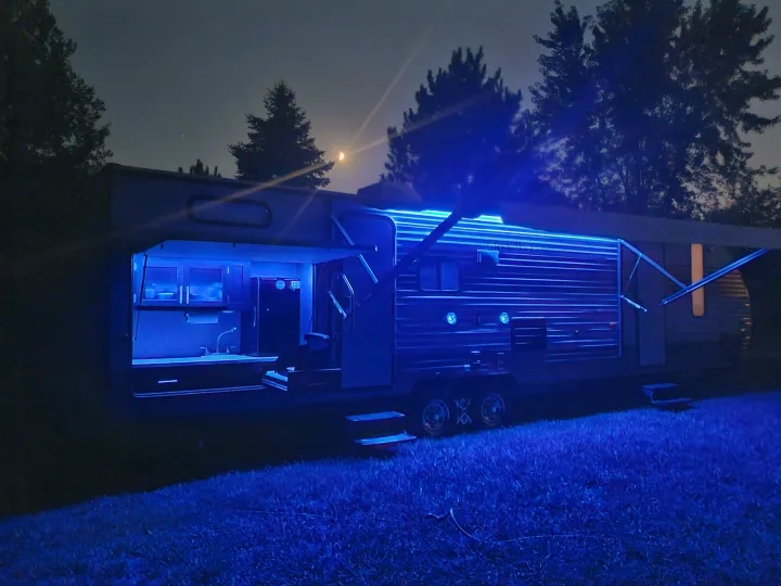 Night view of an **rv rental** with stunning blue LED lighting along the awning and inside its open outdoor kitchen under a moonlit sky.. Forest River Cherokee Grey Wolf 2017