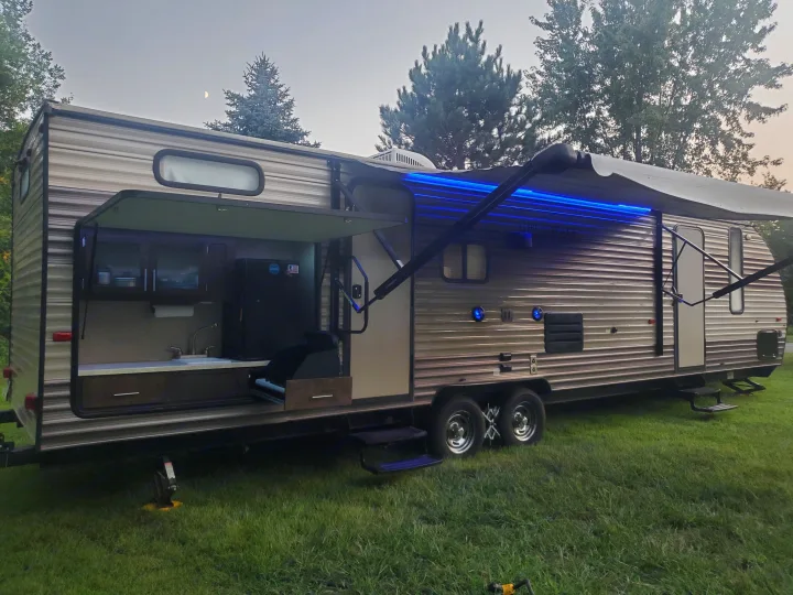 Travel trailer RV rental set up for camping, with its outdoor kitchen pulled out, under a blue-lit awning at dusk.. Forest River Cherokee Grey Wolf 2017