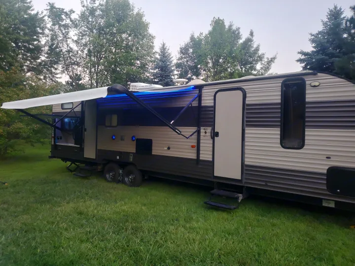 Visually: A travel trailer RV rental parked on grass, with an extended, blue-lit awning and outdoor kitchen.. Forest River Cherokee Grey Wolf 2017