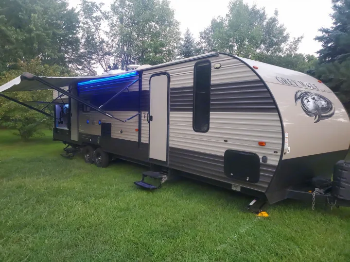 Spacious Grey Wolf RV rental parked on green grass with extended awning and blue lights. Ideal for getaways.. Forest River Cherokee Grey Wolf 2017