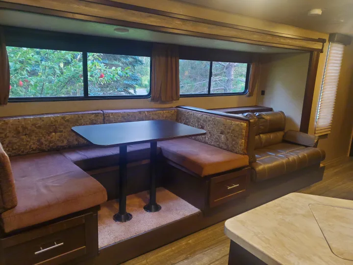 RV rental interior featuring a U-shaped dinette, comfortable seating, and large windows revealing a scenic outdoor view.. Forest River Cherokee Grey Wolf 2017