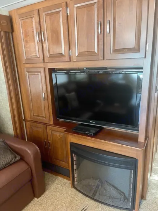 Inside your RV rental: a warm living space with a large TV, electric fireplace, and wood cabinets. Relax in comfort!. Georgetown XL 2013