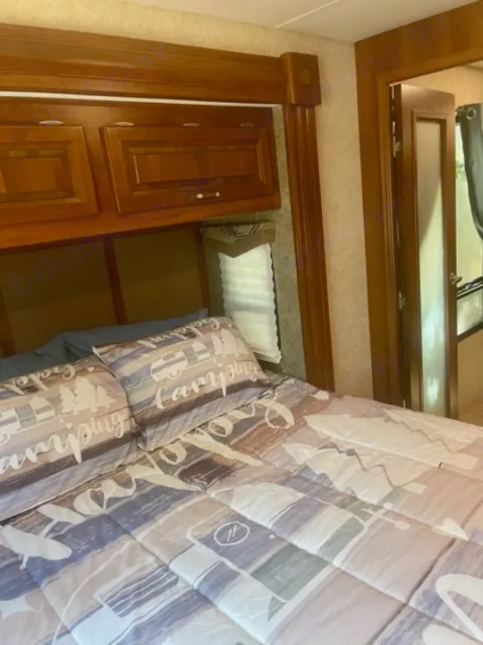 Inside an RV rental bedroom: bed with camping quilt, overhead wood cabinets, and window blinds. Ready for adventure.. Georgetown XL 2013