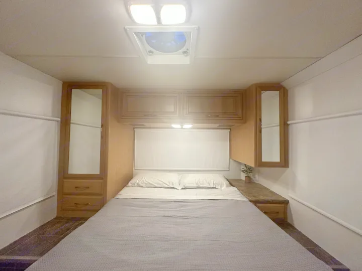 RV rental bedroom interior showcasing a comfortable bed, overhead cabinets, and built-in side storage with mirrors.. Thor Majestic 2012