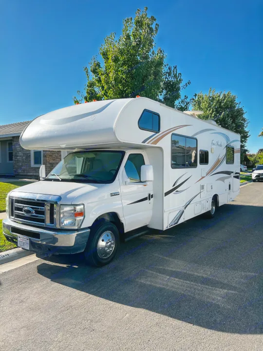 White Class C motorhome with 'Four Winds' branding, a potential rv rental, parked on a sunny street.. Thor Majestic 2012