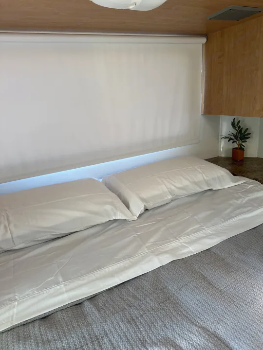 This cozy RV rental bedroom features white bedding, soft blue lighting, and wood cabinetry for a comfortable trip.. Thor Majestic 2012