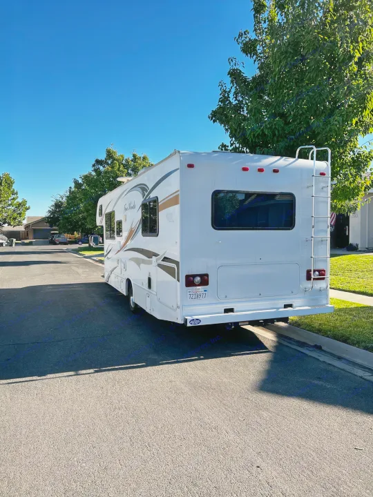 A Class C **rv rental**, white with brown graphics, parked on a sunlit residential street. Ready for your travels.. Thor Majestic 2012