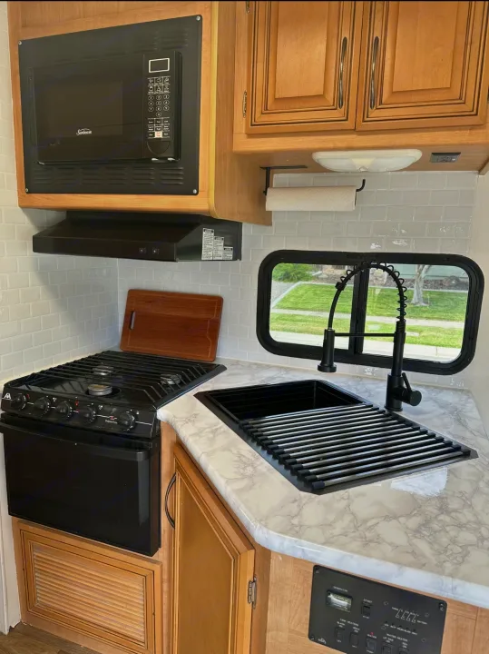 Bright RV rental kitchen showcasing black appliances, a modern sink, and white marble-patterned countertops.. Thor Majestic 2012