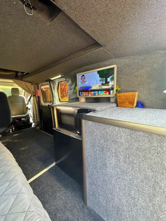 This RV rental's cozy van conversion features a TV, microwave, and gray carpeted interior for mobile comfort.. Ford Transit 2016