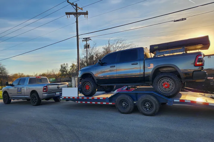 A powerful Ram truck tows an overland adventure rig with a roof tent on a flatbed. Perfect for an RV rental or off-grid trip.. Custom 24ft Buggy Hauler 2023