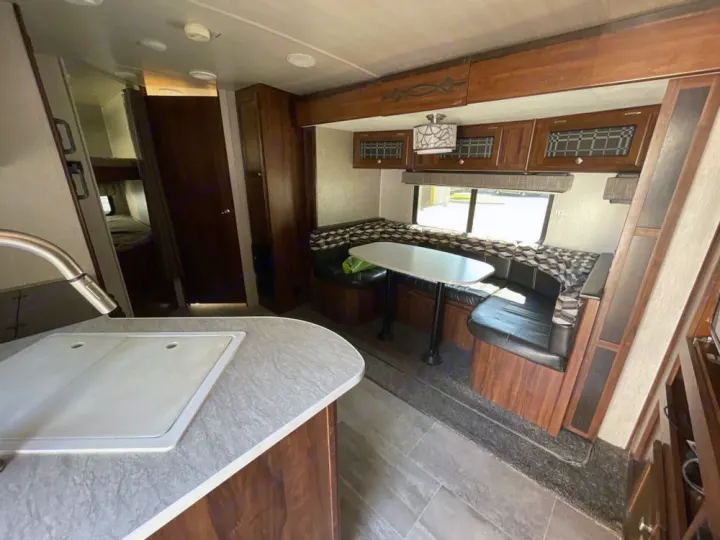This RV rental features a full kitchen in the foreground, a U-shaped dinette, and bunk beds with bathroom access visible.. Heartland RVs Mallard 2018
