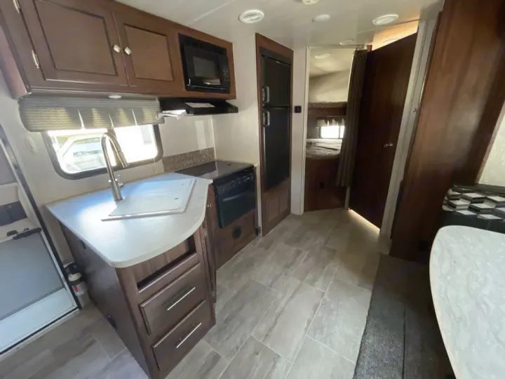 Bright RV rental interior: kitchen with sink, microwave, stove, fridge, and a bunk bed area. Ideal for travel.. Heartland RVs Mallard 2018