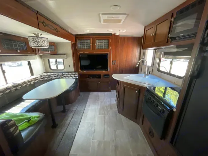 RV rental's inviting interior: dinette, compact kitchen with sink/stove/microwave, TV, & ample wood cabinetry.. Heartland RVs Mallard 2018
