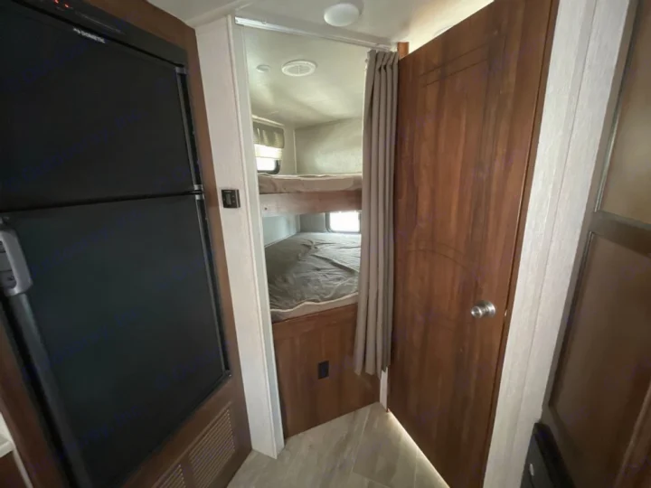Inside this RV rental, a black refrigerator stands next to bunk beds, offering compact sleeping space.. Heartland RVs Mallard 2018