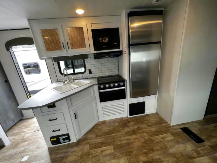 Modern RV rental: Bright kitchen with white cabinets, subway tile, stainless appliances, sink, and wood floors.. Keystone Hideout 2022