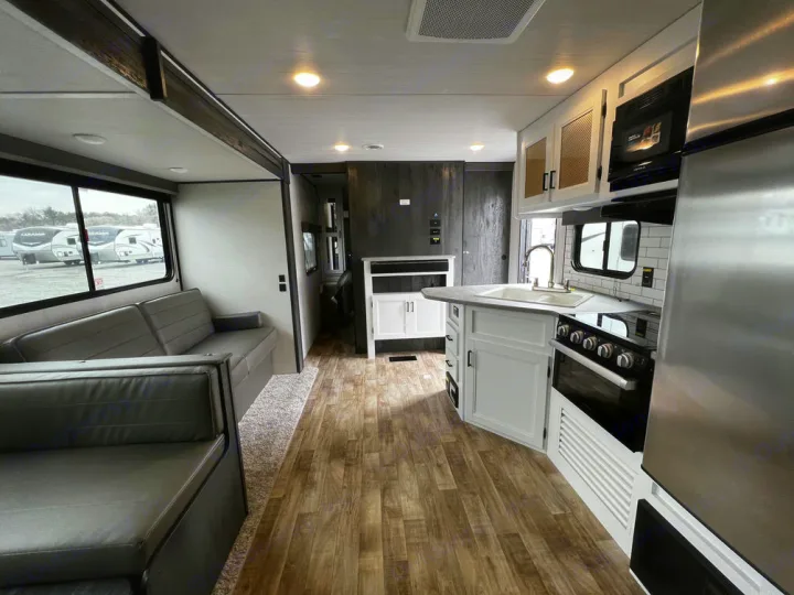 Modern RV rental interior: spacious kitchen with white cabinets, living area with sofa, and wood floors.. Keystone Hideout 2022