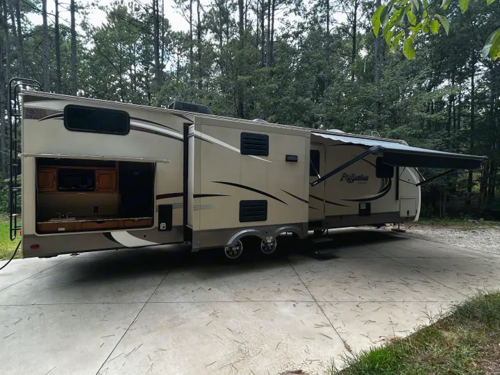 Spacious RV rental with outdoor kitchen, awning extended, parked on concrete in woods. Ideal for glamping!. Grand Design Reflection 2015