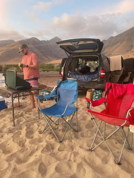 Man preparing food by a car camping setup with mountains & sand. Ideal for an outdoor adventure, like an RV rental trip.. Xplorer Explorer 2007