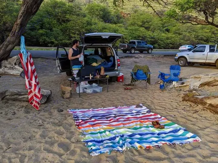 Car camping beside the road on sand. A person unpacks, with chairs and a colorful blanket out. An RV rental-style stop.. Xplorer Explorer 2007