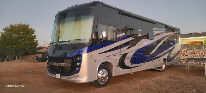 A large, modern Entegra Vision XL RV in blue, silver, and black is parked on a dirt surface, ready for rv rental.. Entegra Coach Vision XL 2020