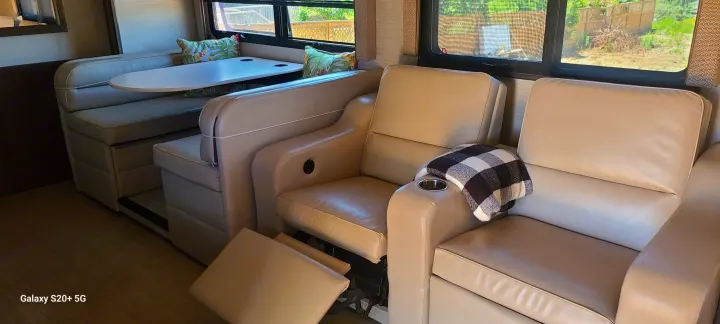 RV rental living space: dinette with table, two light leather recliners (one with extended footrest) by bright windows.. Entegra Coach Vision XL 2020