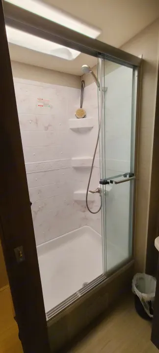 Bright and compact shower in an RV rental, featuring a glass door, built-in shelves, and white marble-look walls.. Entegra Coach Vision XL 2020