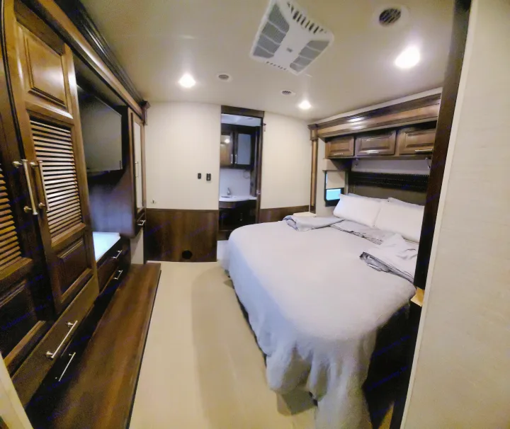 Well-appointed RV rental bedroom. Features a large bed, dark wood cabinetry, and an ensuite bath area.. Entegra Coach Vision XL 2020