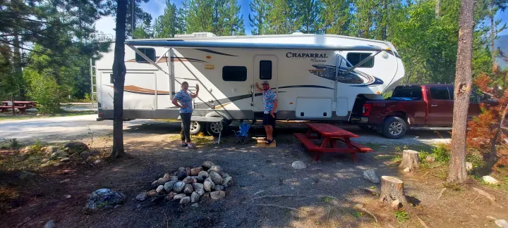Couple with RV rental at their forest campsite, complete with picnic table and fire pit, enjoying the outdoors.. Forest River Coachmen 2012