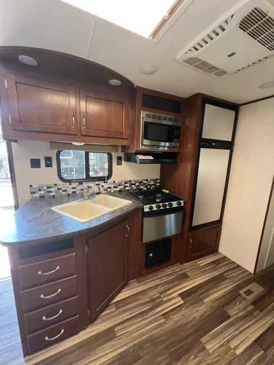 Experience the full kitchen of this RV rental, featuring dark wood cabinets, sink, microwave, and stove.. Jayco Jay Flight 2017