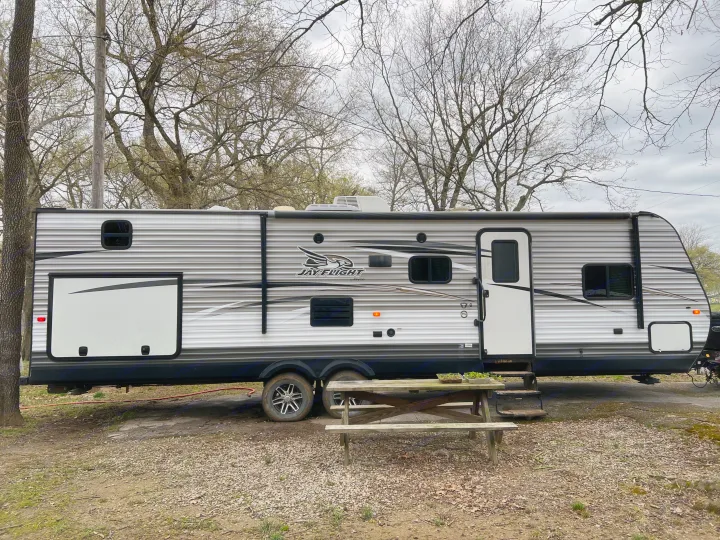Jayco travel trailer RV rental parked at a wooded campsite with a picnic table.. Jayco Jay Flight 2017