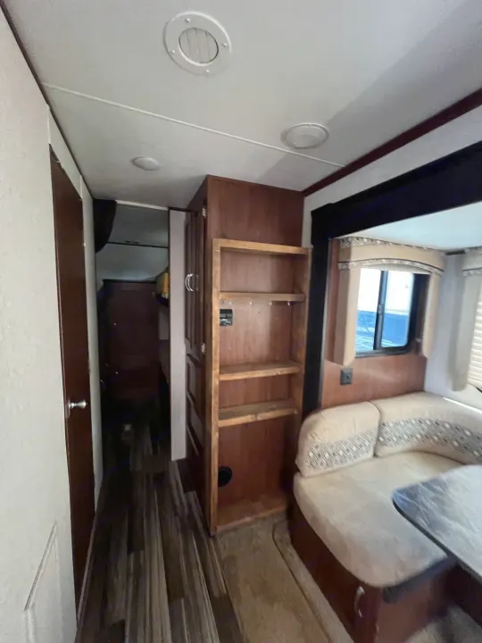 Bright RV rental interior with a cozy U-shaped dinette, wood-look flooring, built-in shelves, and a large window.. Jayco Jay Flight 2017