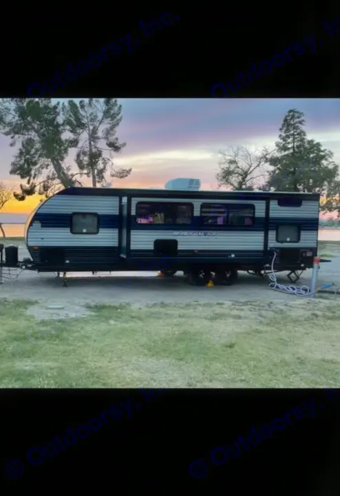Enjoy an RV rental: a modern travel trailer with colorful interior lights, set against a stunning lake sunset.. Forest River Cherokee Grey Wolf 2021