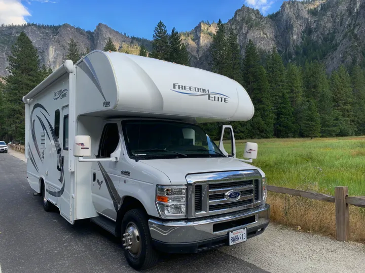 White Ford Freedom Elite RV rental parked by mountains & forest. Ideal for scenic adventures.. Thor Freedom Elite 2019