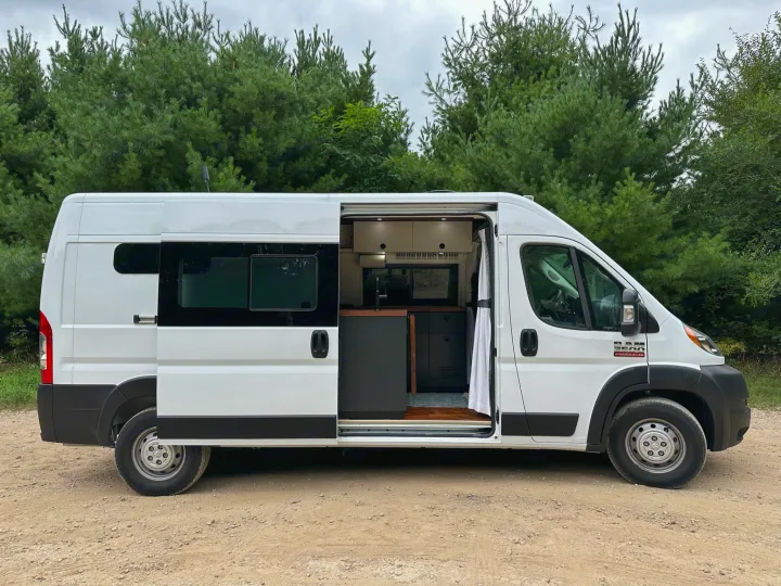 White Ram ProMaster rv rental van with side door open, revealing its custom camper interior. Parked on a dirt road.. RAM ProMaster 2500 2022