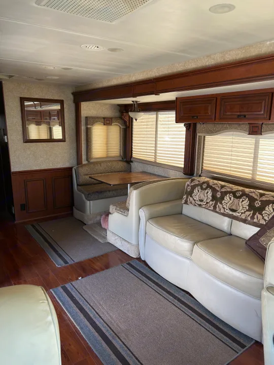 Inside a comfy RV rental: spacious living area with dinette booth, sofa, rich wood cabinetry & warm lighting.. Four Winds Windsport 2010