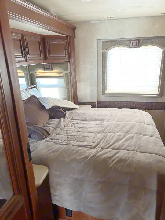 Cozy RV rental bedroom with a comfy bed, overhead cabinets, and bright windows, perfect for relaxation on the road.. Four Winds Windsport 2010