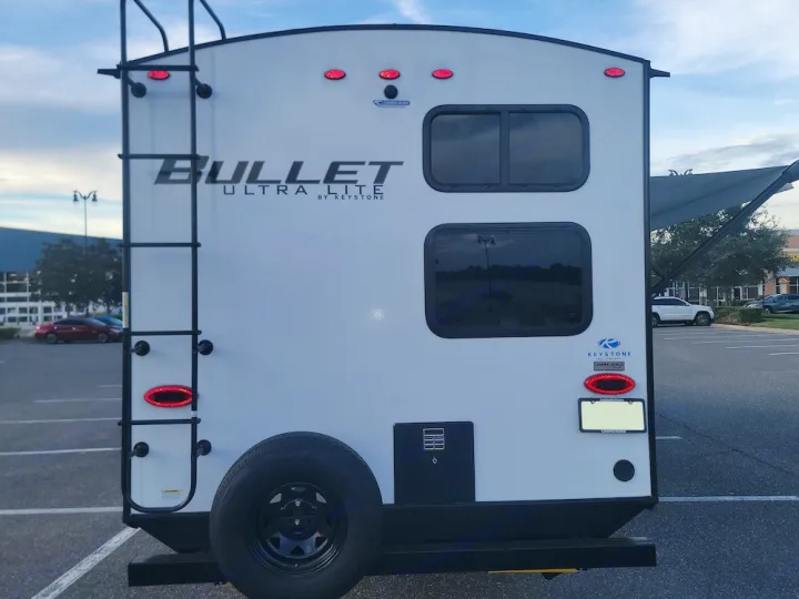 This white Bullet Ultra Lite RV travel trailer, equipped with a ladder and spare tire, is perfect for your rv rental camping trip.. Keystone RV Bullet Ultra Lite 2023