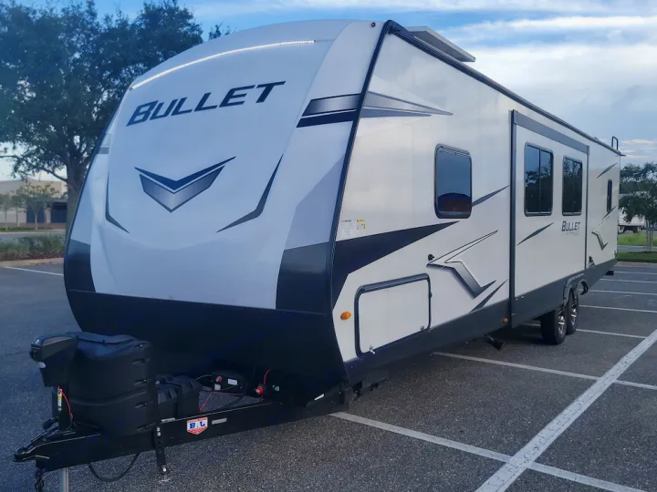 White "BULLET" travel trailer for rv rental, featuring black accents, is parked in a lot. Seen from the front.. Keystone RV Bullet Ultra Lite 2023