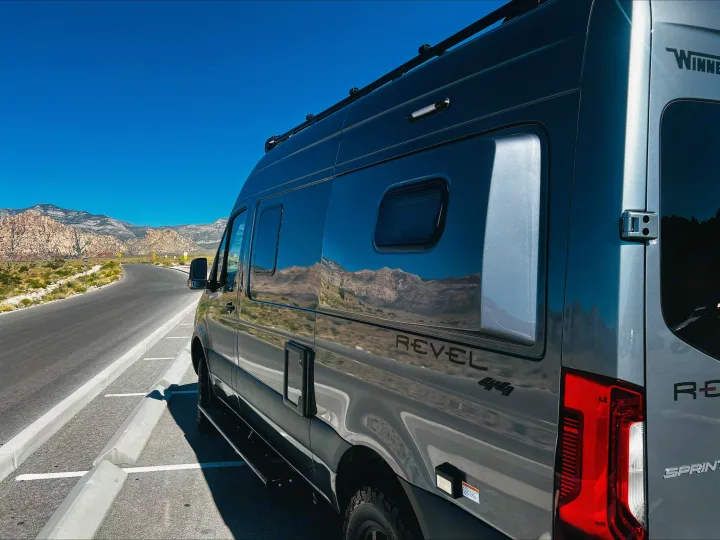 Gray Winnebago Revel 4x4 RV rental parked on a scenic desert mountain road, reflecting the blue sky and mountains.. Mercedes Winnebago Revel 2024