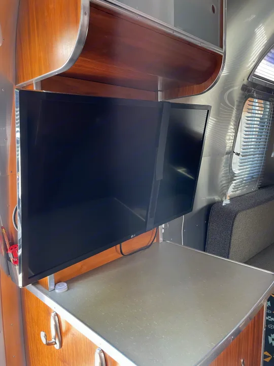 RV rental: Dual black screens mounted above a grey countertop, framed by warm wood cabinetry and polished aluminum trim.. Airstream International 2007